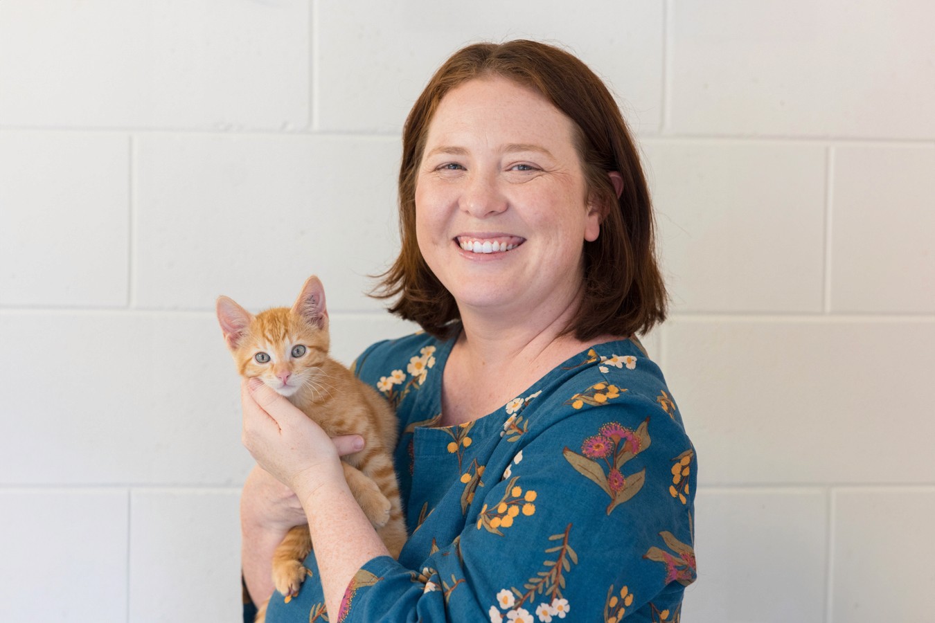 Woman in turquoise dress holding ginger kitten