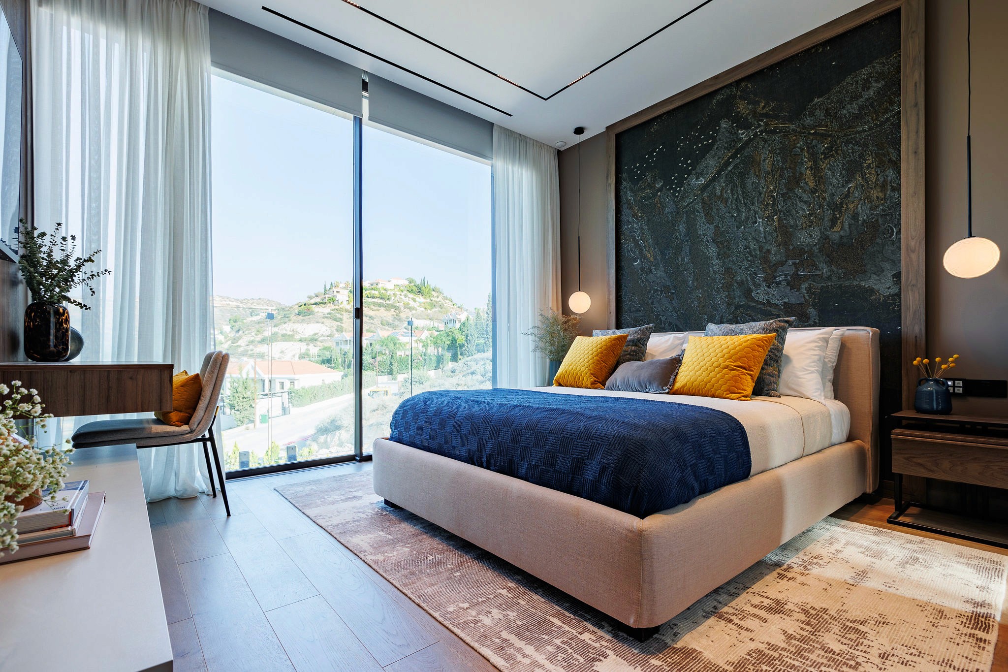 Villa Trio bedroom with textured feature wall, upholstered bed, and floor-to-ceiling glazing with hillside views