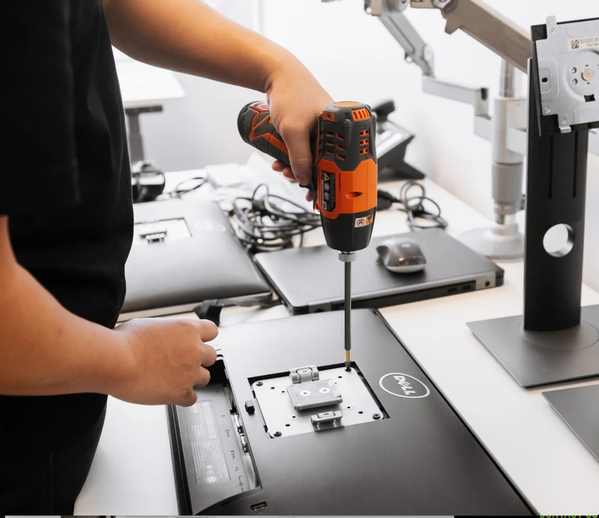 Technician using a power drill to install or remove a monitor mount on a Dell display in an office IT setup environment