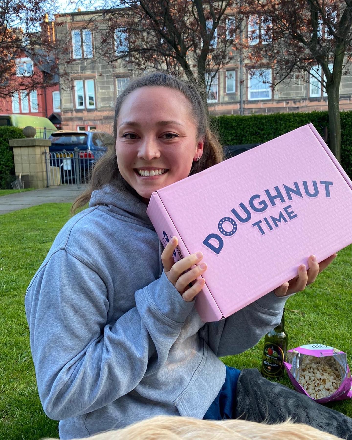 Tsui wearing a grey hoodie, holding a box of Doughnut Time doughnuts in a garden