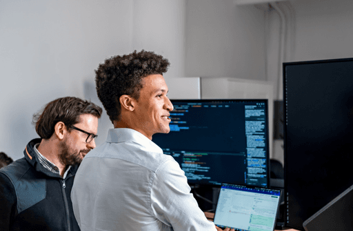 Two smiling male developers collaborate in a modern office, focusing on a digital product displayed across multiple screens.
