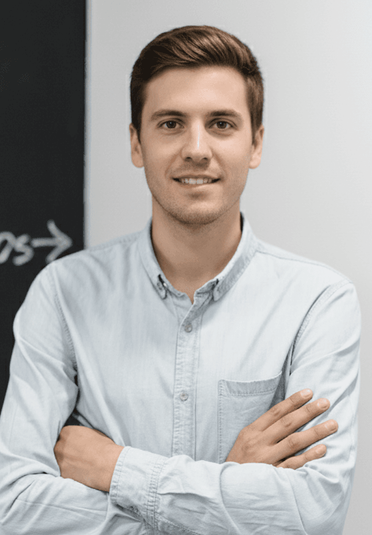 Male scientist in a white lab coat standing confidently in a modern hydroponic lab with pink grow lights and rows of leafy greens.