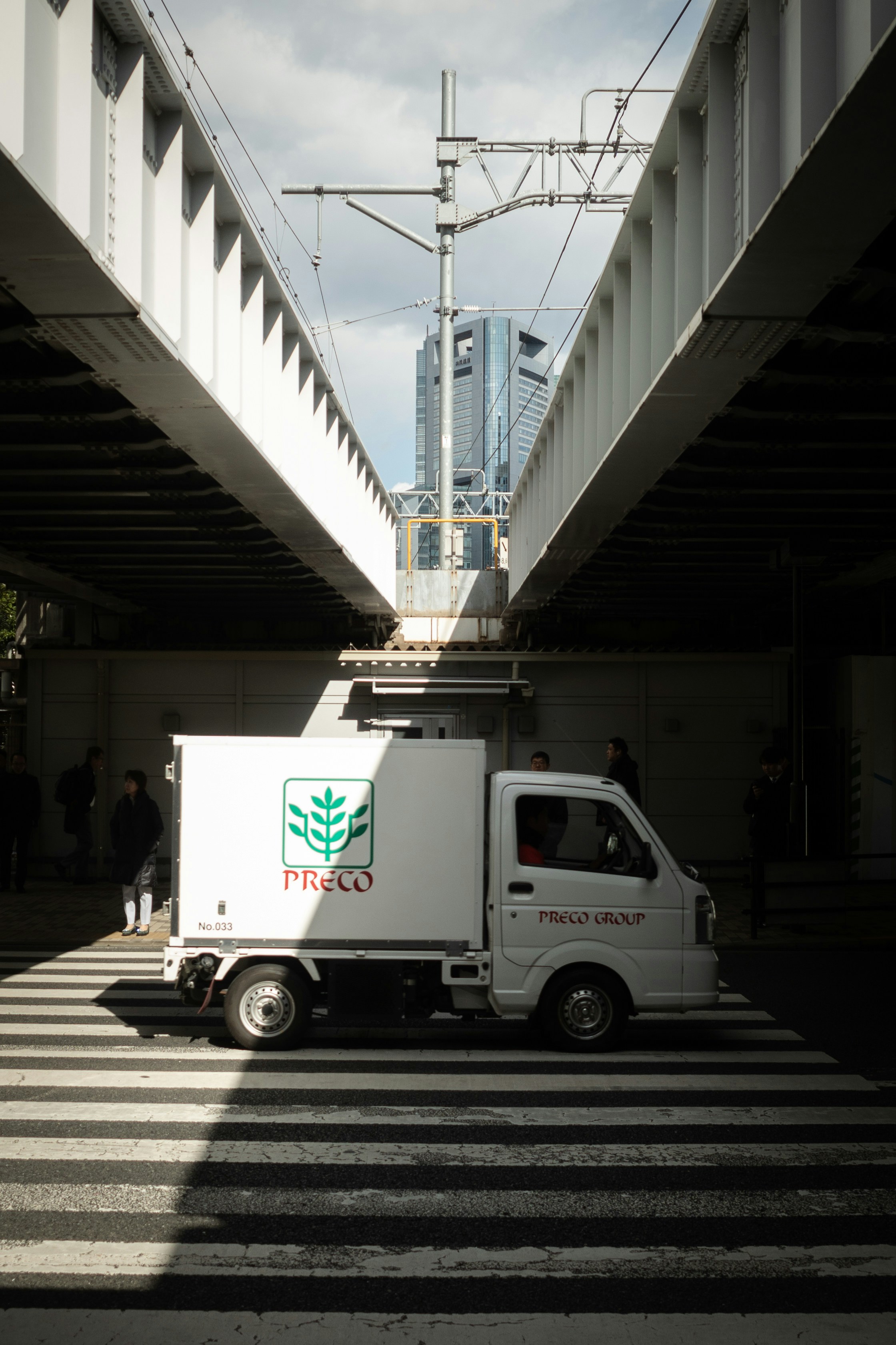 White delivery truck on a crosswalk under railway bridge.
