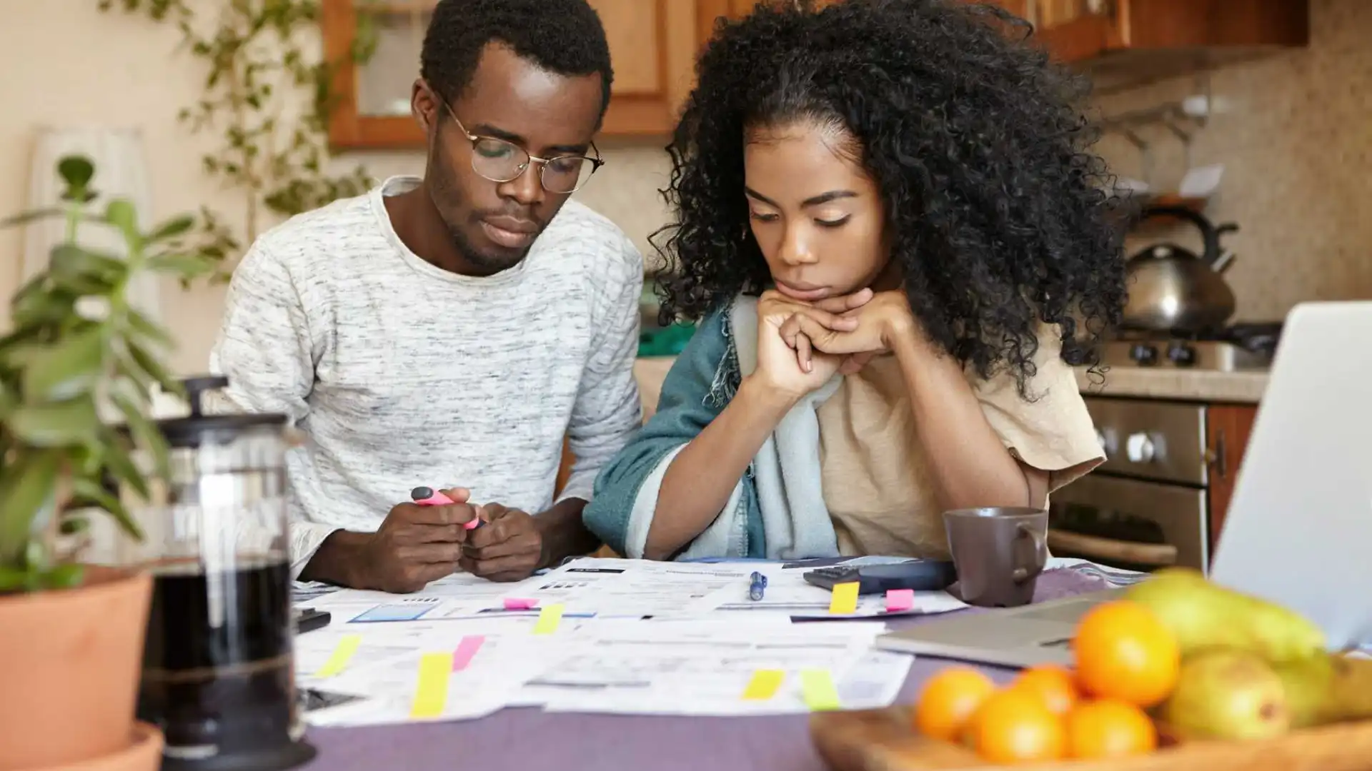 Een stel zit aan de keukentafel bezig met papieren, fruit en een laptop in de buurt.