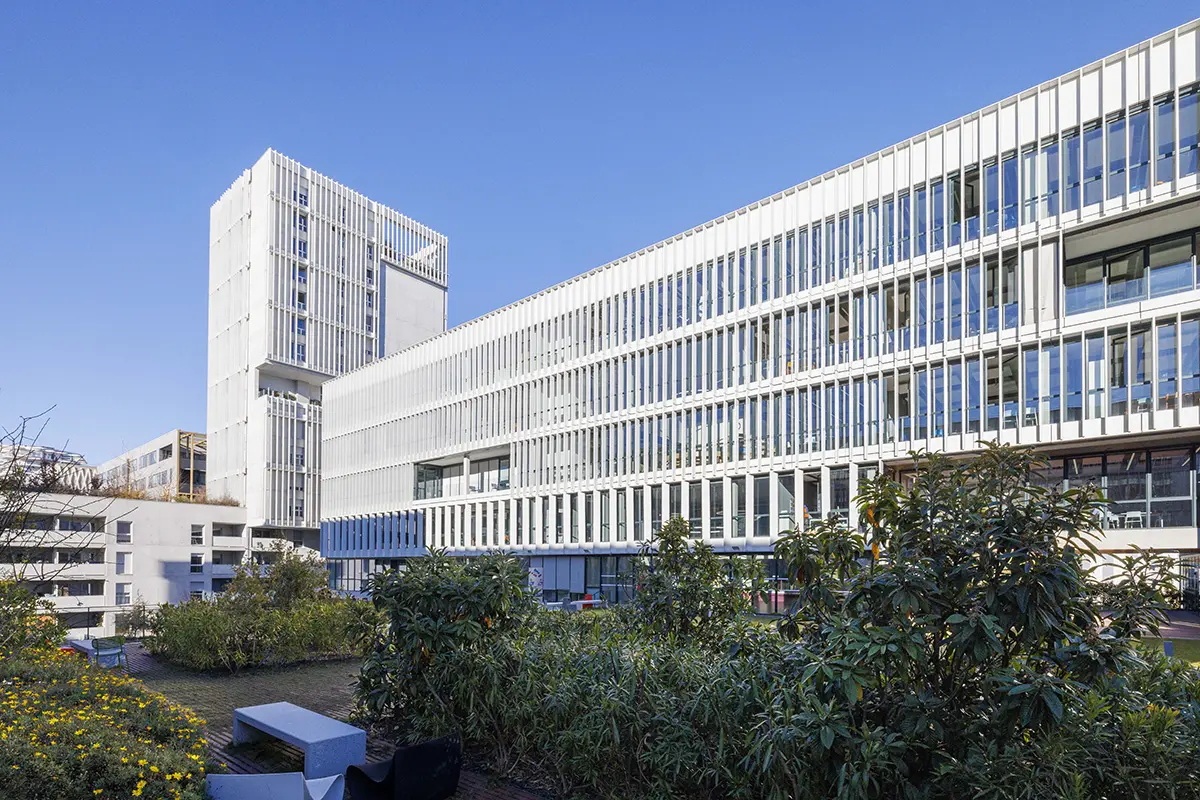 Au coucher du soleil, un bâtiment moderne et blanc de plusieurs étages portant les enseignes "CHU" et "CHAUDET" se détache des bâtiments plus anciens de la ville portuaire, avec des navires et des grues visibles au loin.