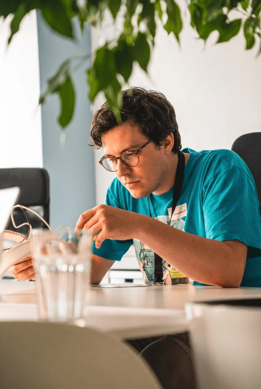 Person in türkisfarbenem T-Shirt sitzt an einem Tisch und hält einen Hardware Prototypen in der Hand
