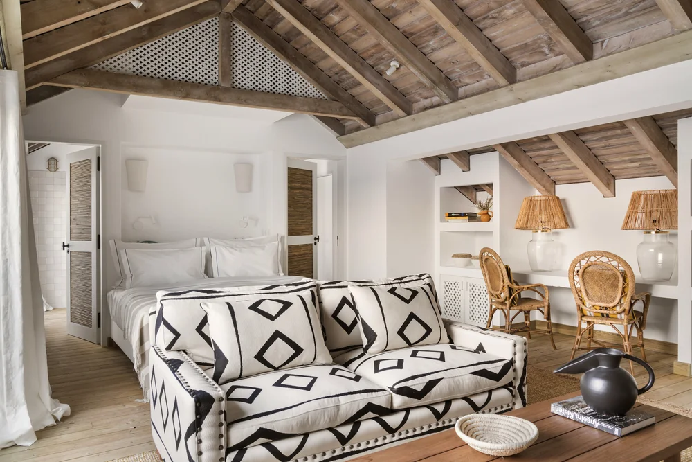 Helles Schlafzimmer mit Holzbalkendecke, Sofa mit schwarz-weißem Muster und zwei Korbstühlen. Einladendes Interieur.