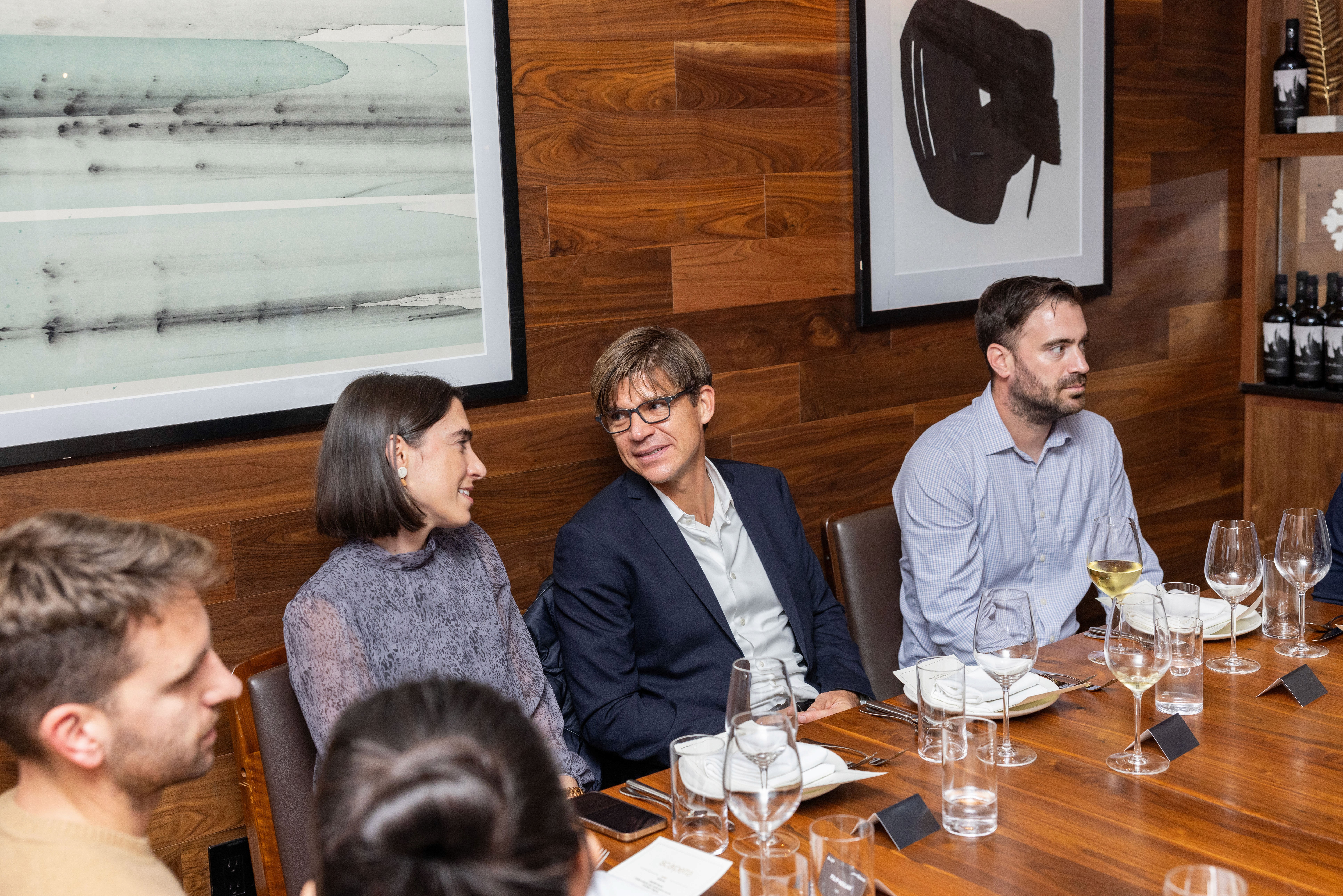 A group of people seated at a wooden table, engaged in conversation in a modern setting.