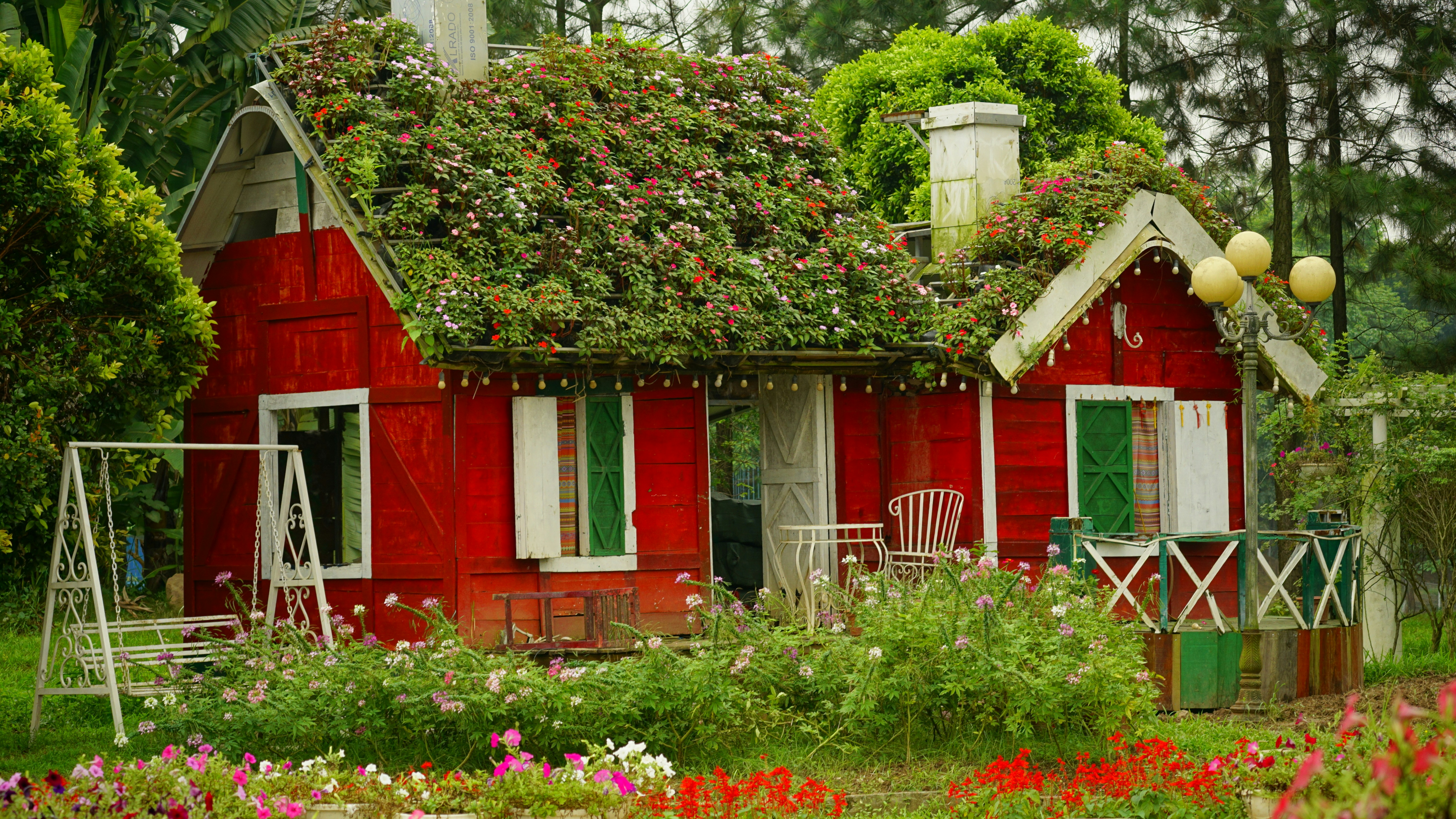 a red house with a green roof surrounded by flowers