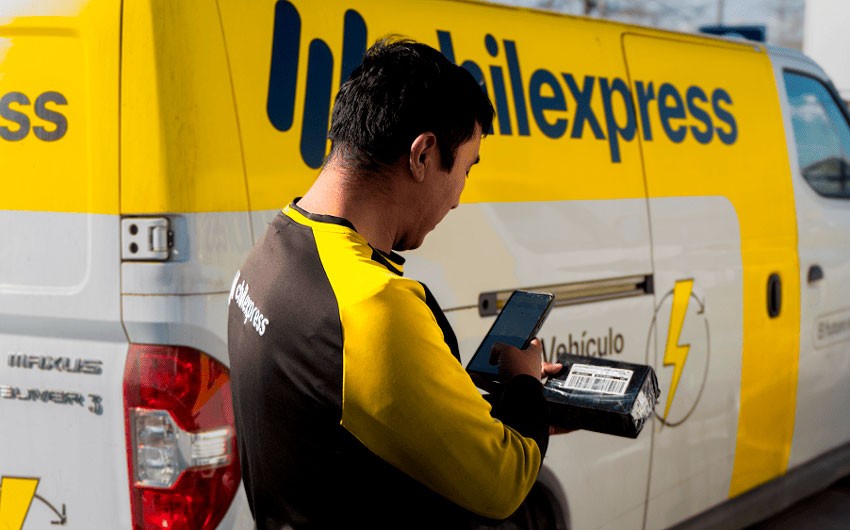 Two colleagues at a whiteboard, one pointing and explaining a concept while the other listens, both dressed in business attire in a modern office space.