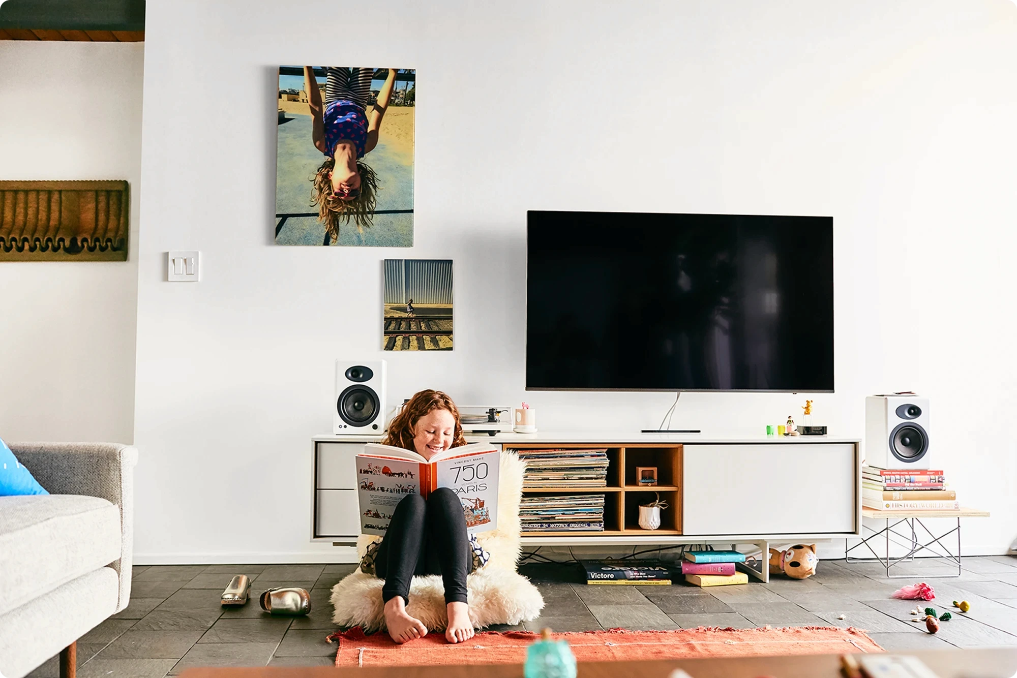 Girl reading on a sheepskin pouf below Fracture prints in a lived-in living room