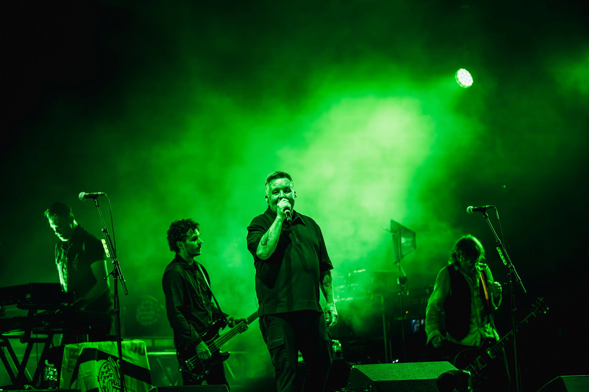 Les Dropkick Murphys sur scène sous une lumière verte intense, avec le chanteur au centre et les musiciens autour de lui.