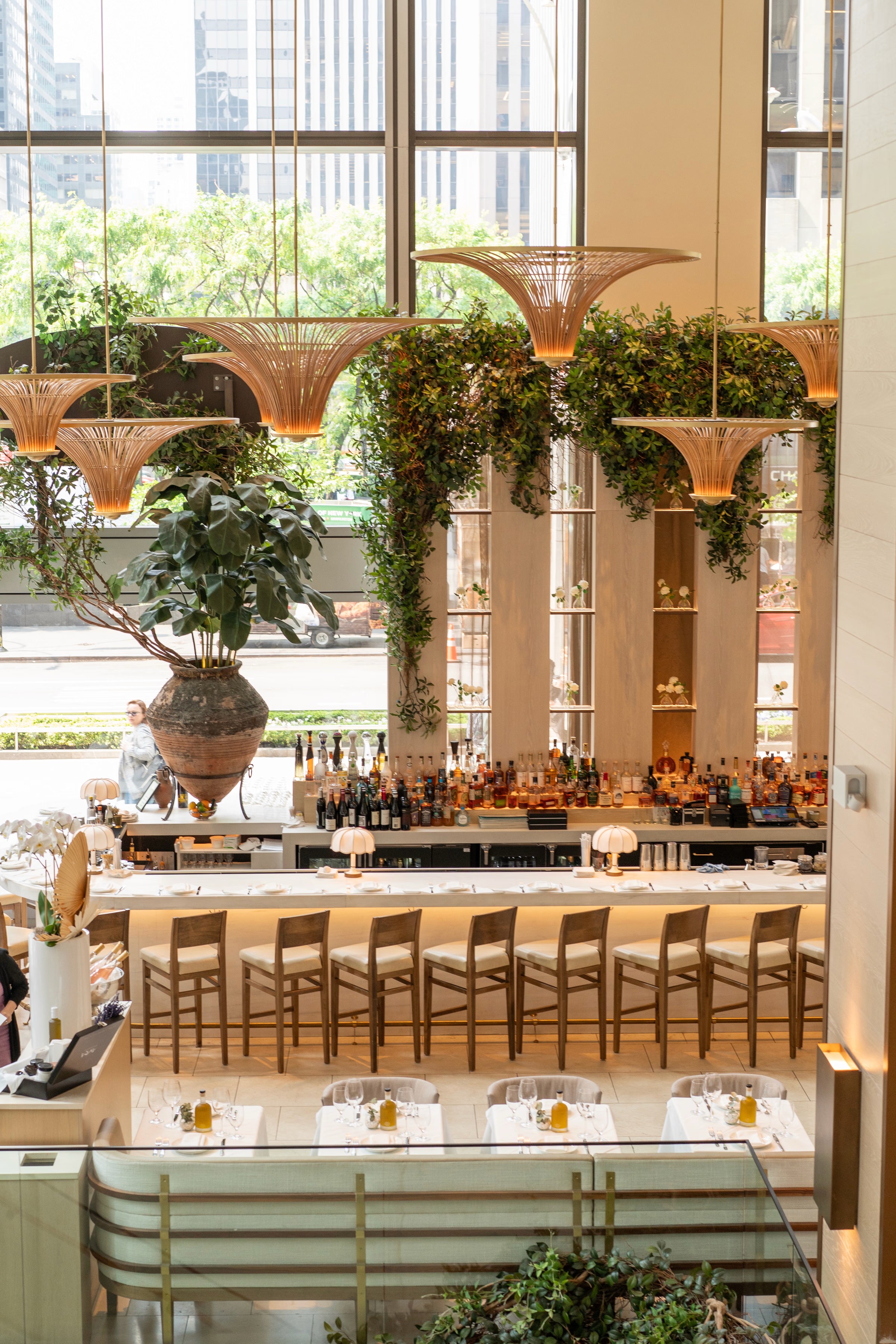 A bright indoor space with large windows, featuring greenery and a cozy seating area.