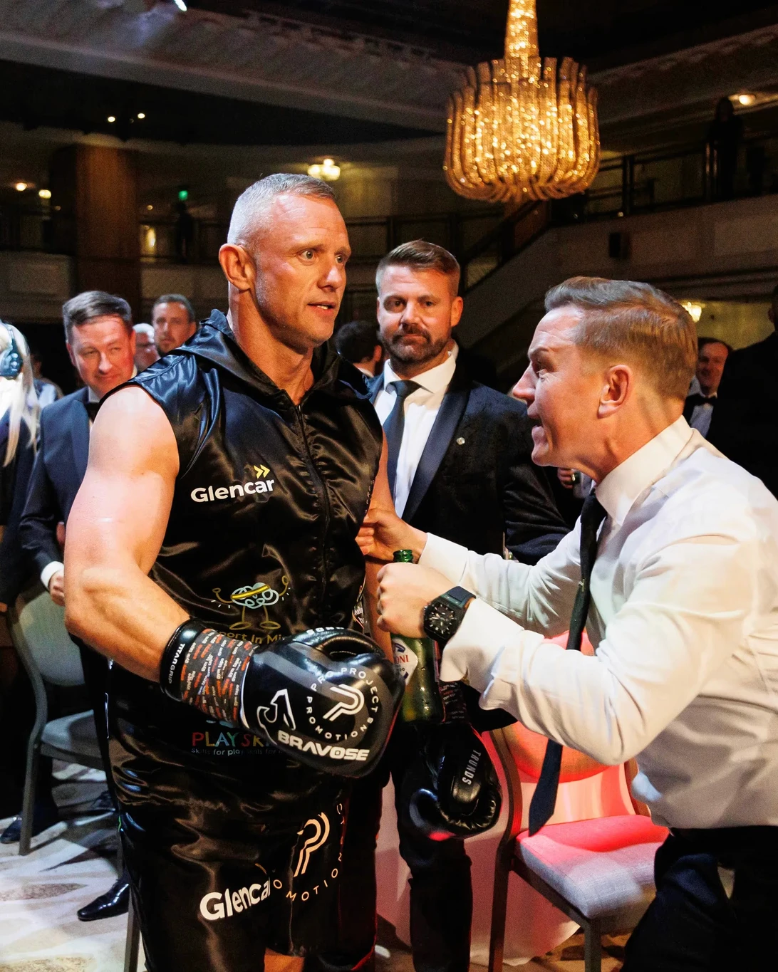 Boxer in black silk outfit, receiving a drink.