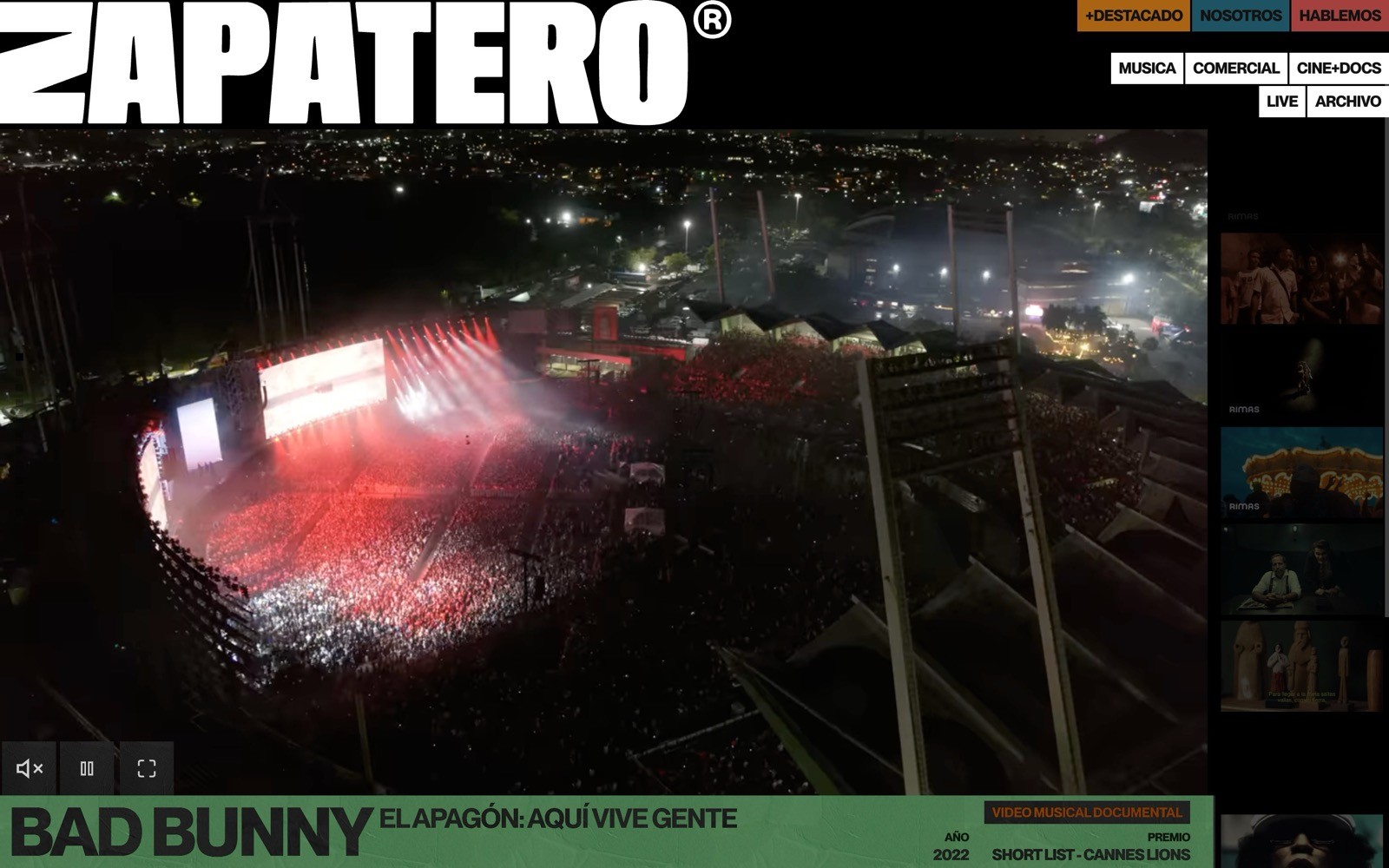 Aerial view of a large outdoor concert at night, stage lit in red, city lights in the background. Text: "ZAPATERO", "BAD BUNNY".