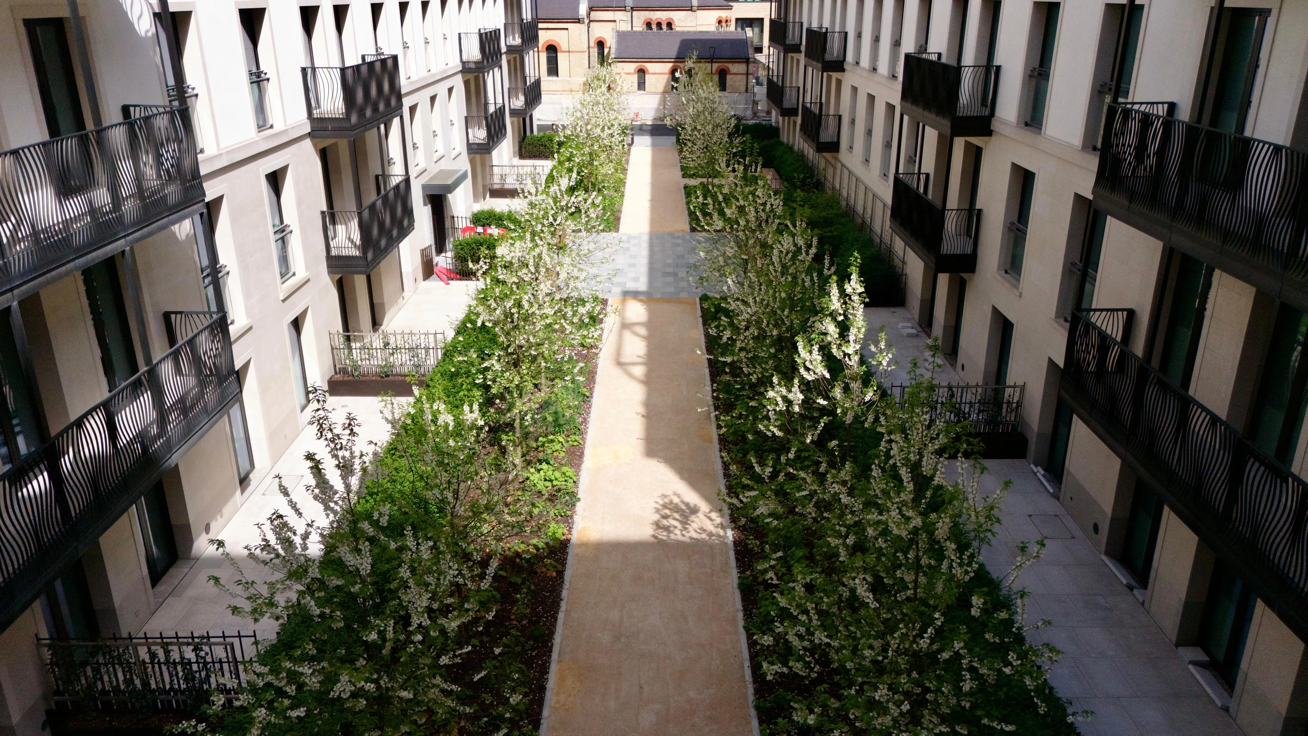 View of a modern courtyard with a central pathway surrounded by greenery and apartment buildings on either side.