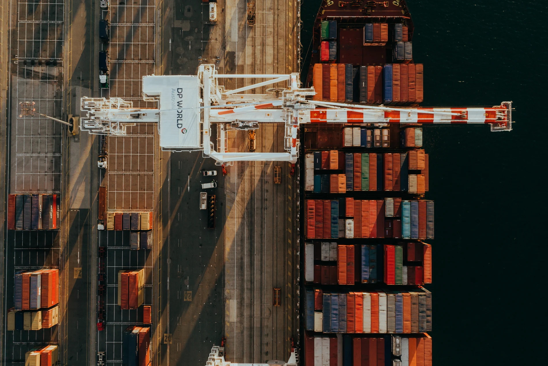 Aerial looking straight down on a wharf crane between long rows of stacked containers