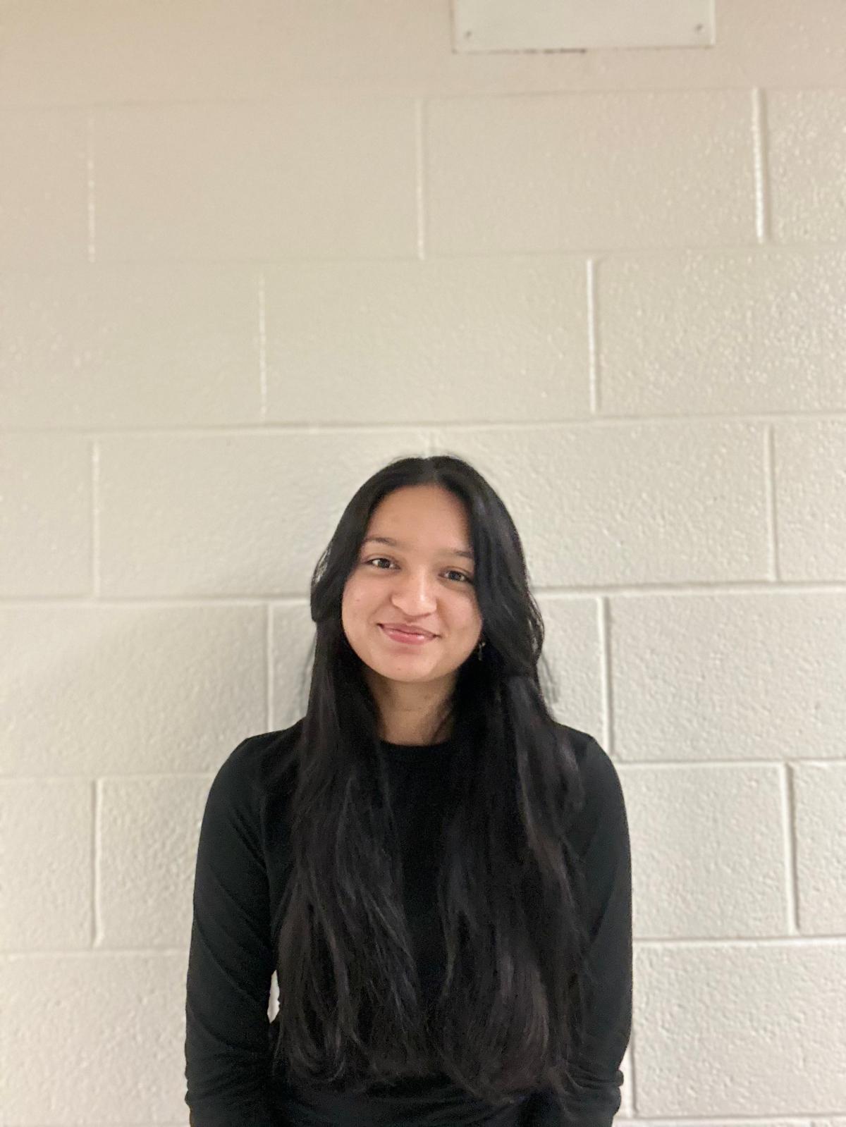 Smiling person with curly hair, wearing a black shirt, against a warm, dark background.