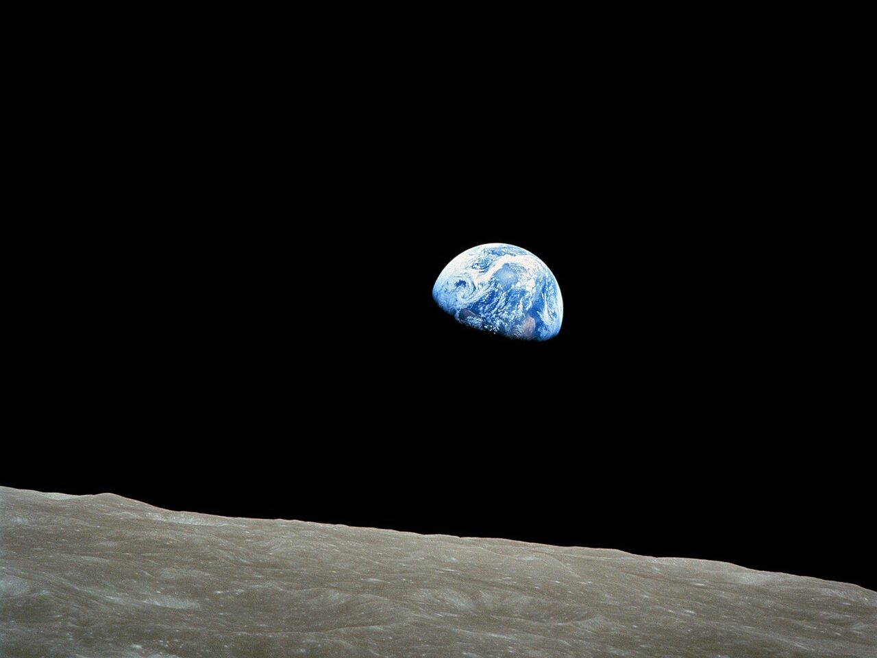 View of Earth rising above the surface of the Moon against the blackness of space.