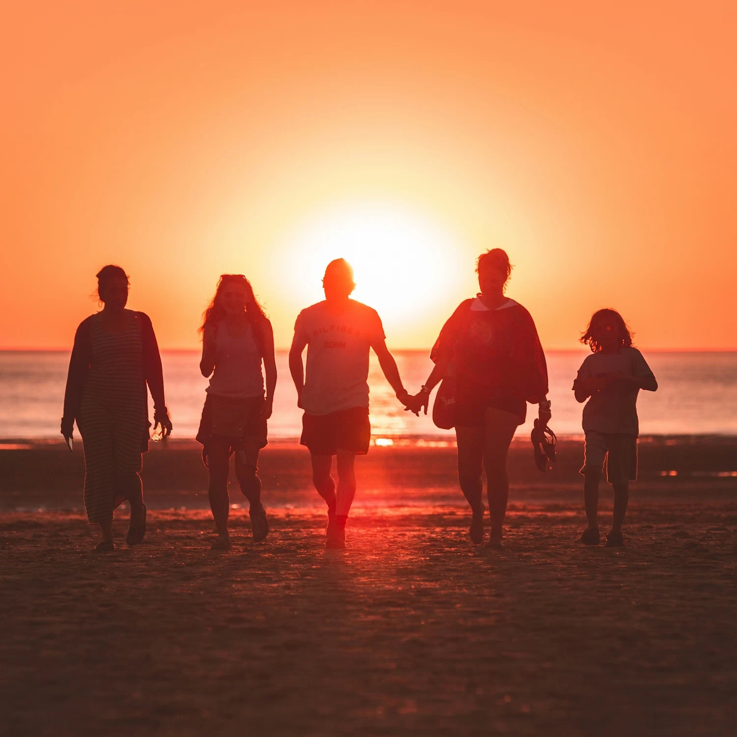 Silhouette of a diverse family walking together on the beach at sunset, representing unity, acceptance, and connection in LGBTQ+ family therapy in Los Angeles.