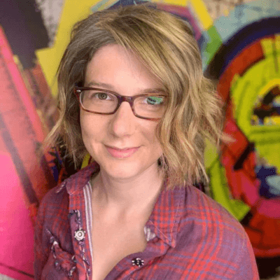 Alt tag: Portrait of Sara Jane Walsh, creator of the Here’s Hope Project and podcast, wearing glasses and a red plaid shirt, smiling softly in front of a colorful abstract mural background.