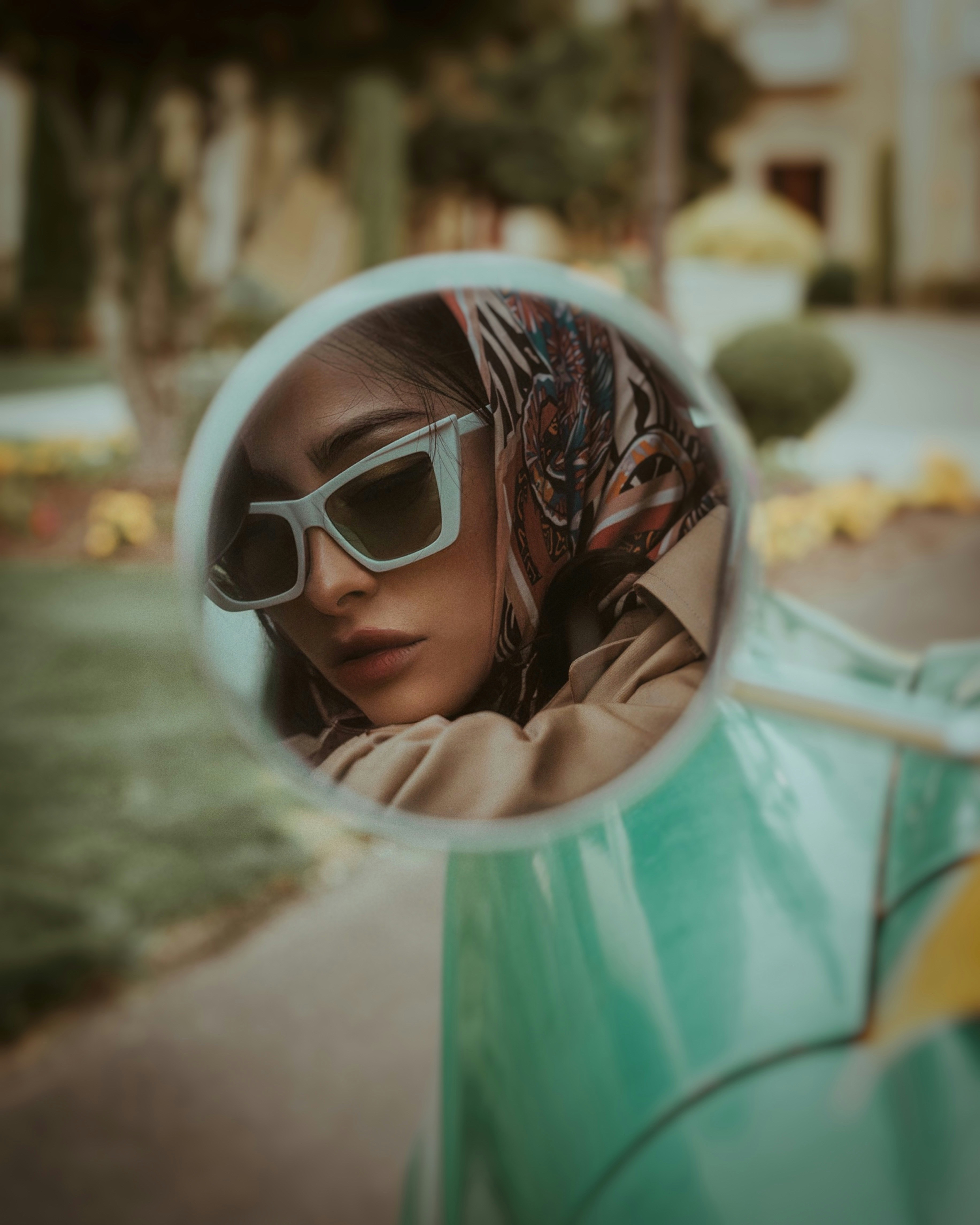 A girl in white cat-eye glasses was looking into the side mirror of a car.