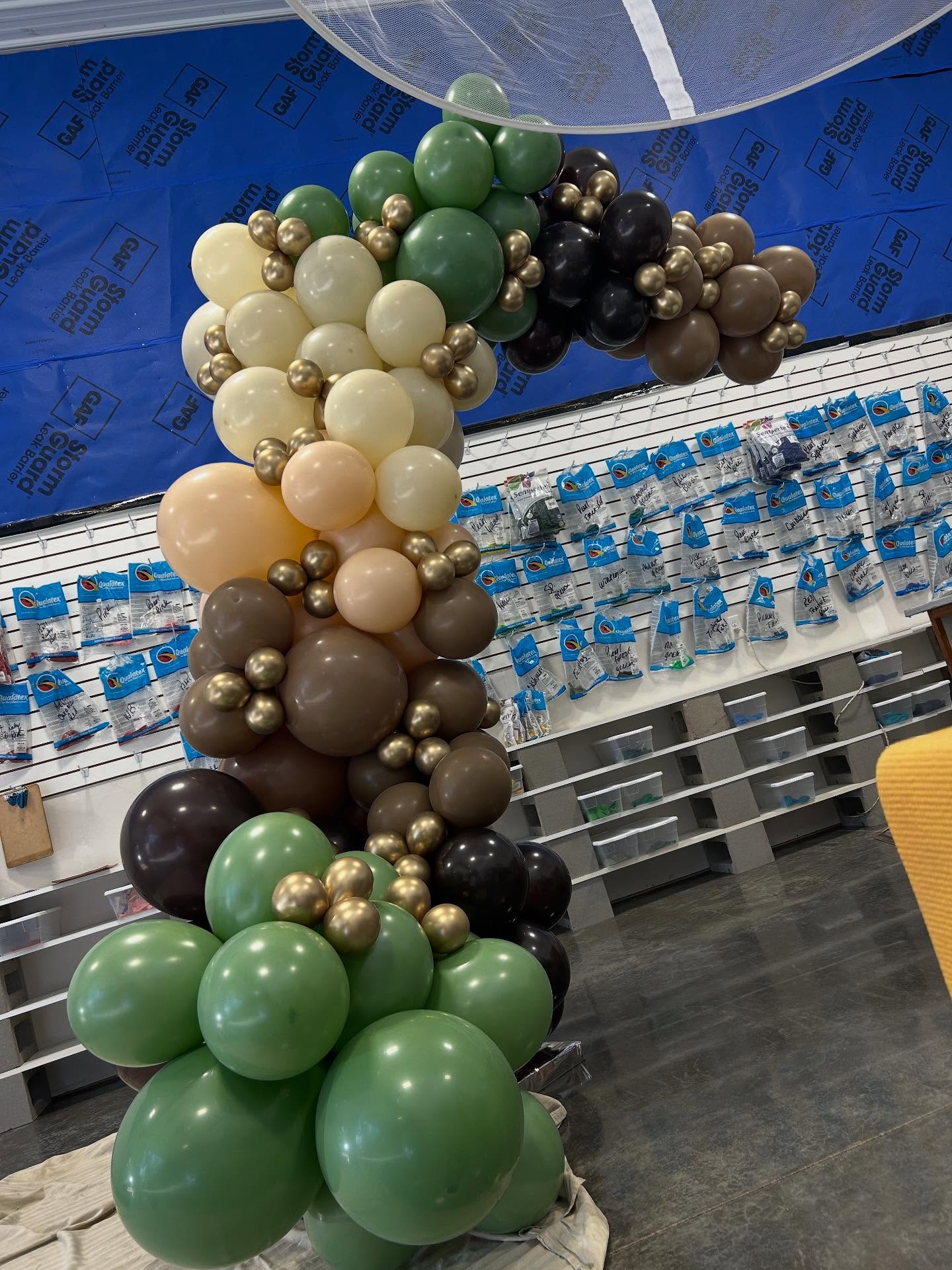 Earth-toned balloon garland with green, brown, beige, and gold balloons arranged along a table by Be Bold Balloons