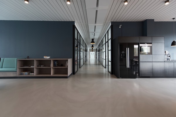 Office interior looking down a corridor of glass-walled rooms past a shared kitchen counter