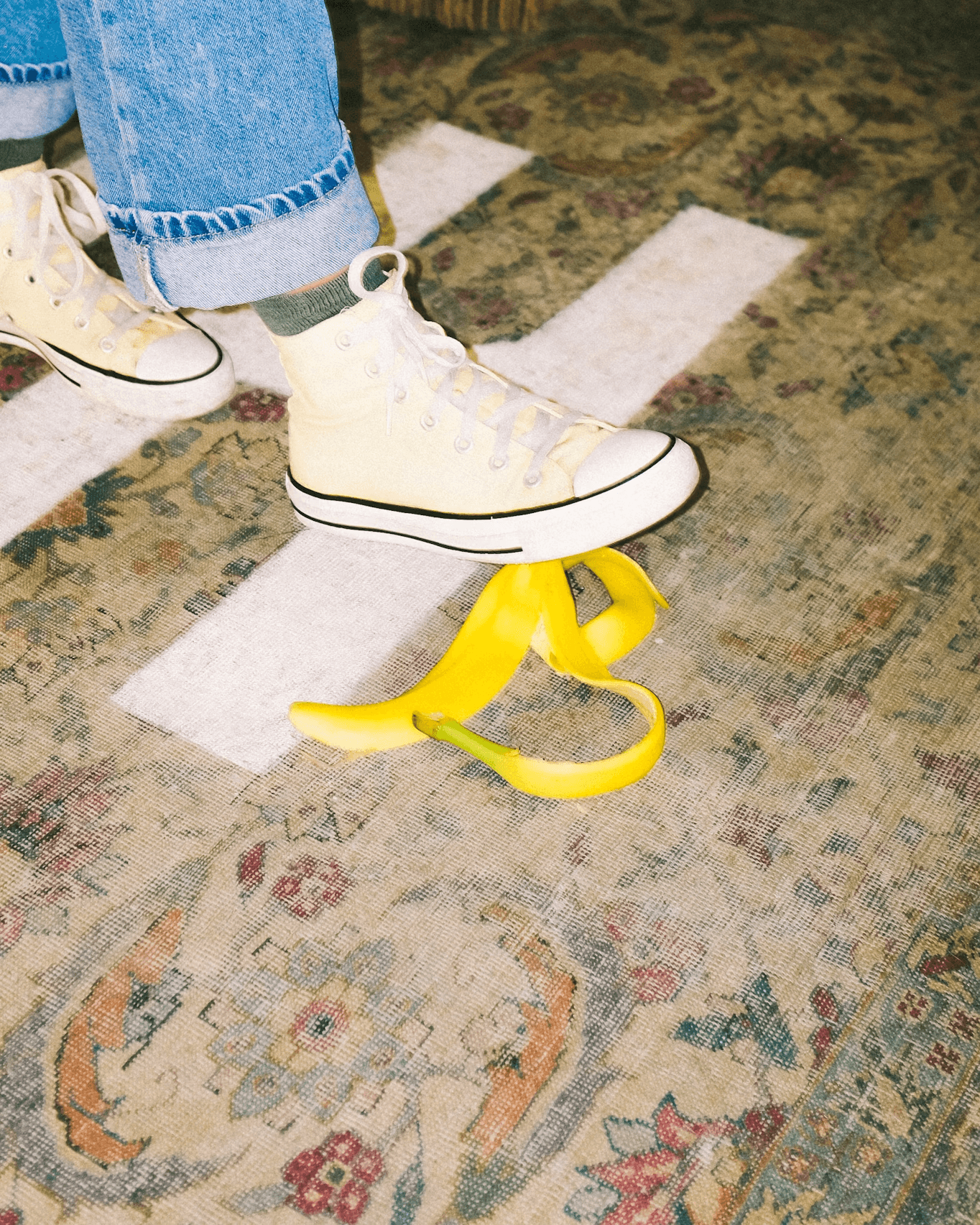 Close-up of a white sneaker stepping on a banana peel on a patterned floor.