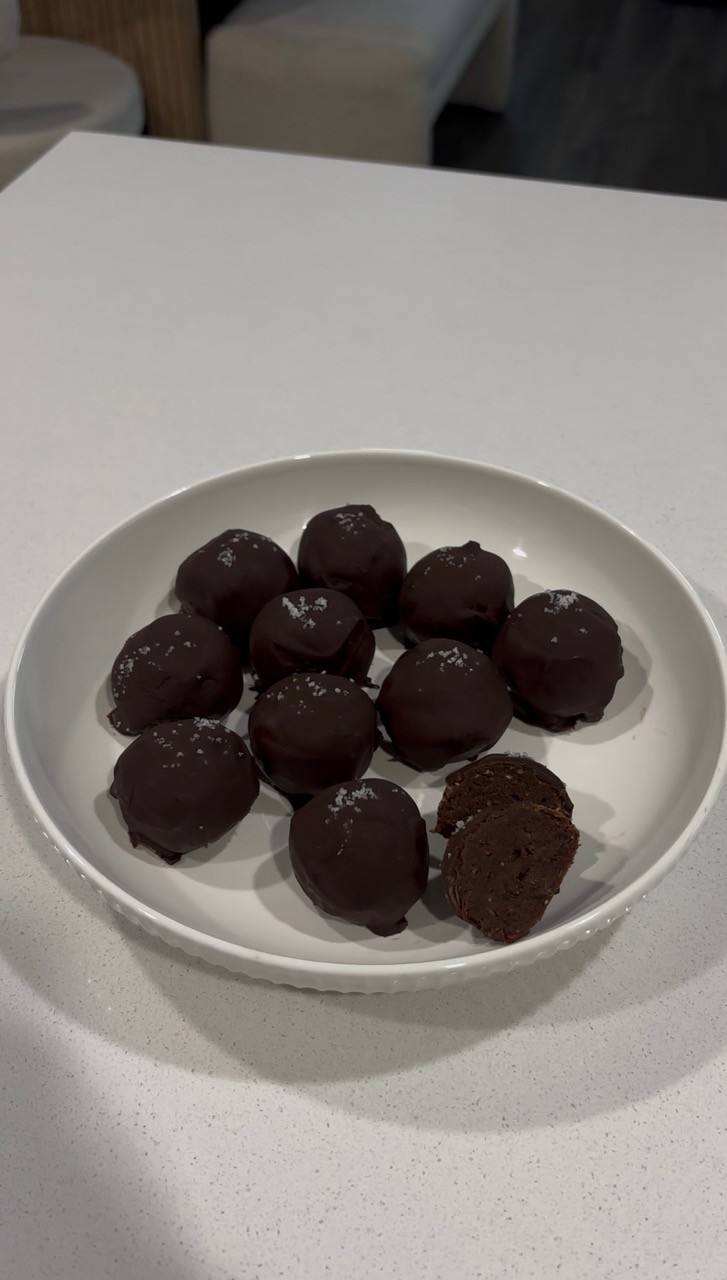 Plate of dark chocolate covered brownie date balls sprinkled with sea salt – refined sugar free chocolate dessert bites Wellness by Suhey