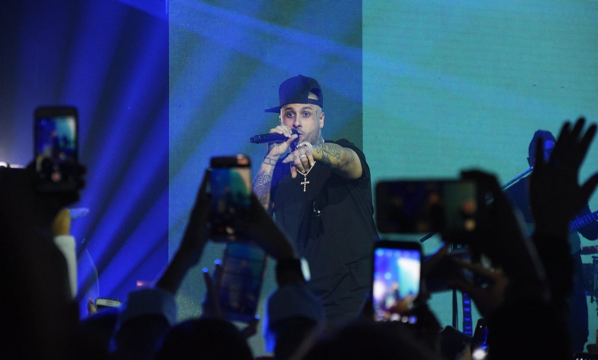 Pareja sentada en cama dentro de cápsula transparente colgada a un acantilado rocoso; otras cápsulas y paisaje nevado abajo.