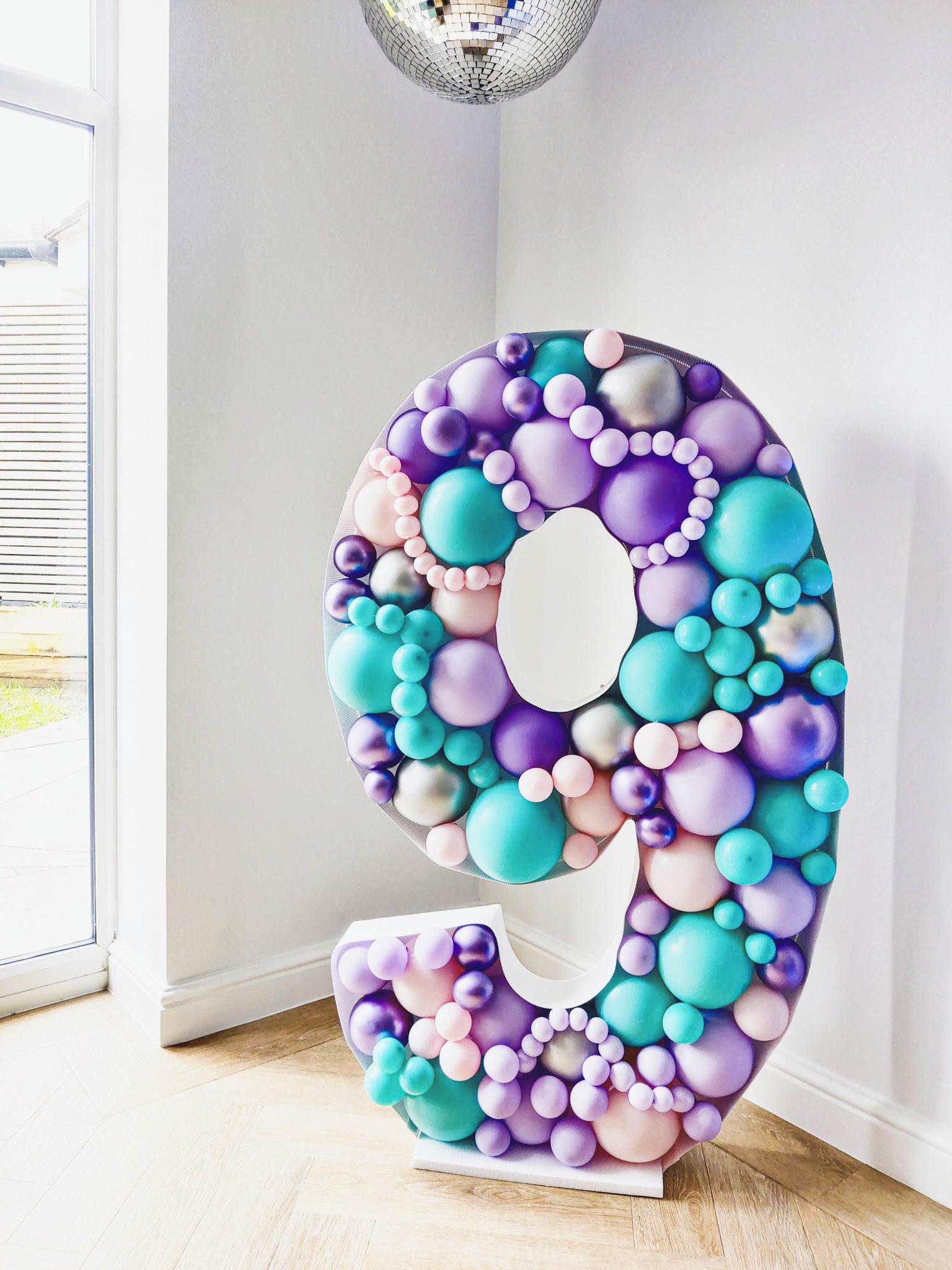Large freestanding number 9 balloon sculpture in turquoise, purple, and pink tones
