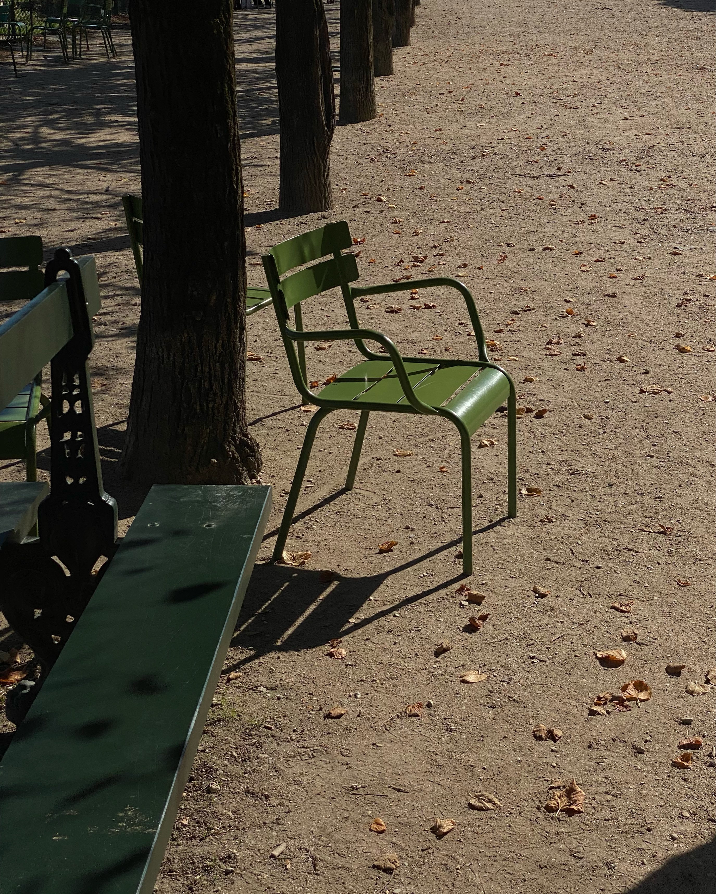 A green chair in a park i Paris casting shadow from the sunshine.