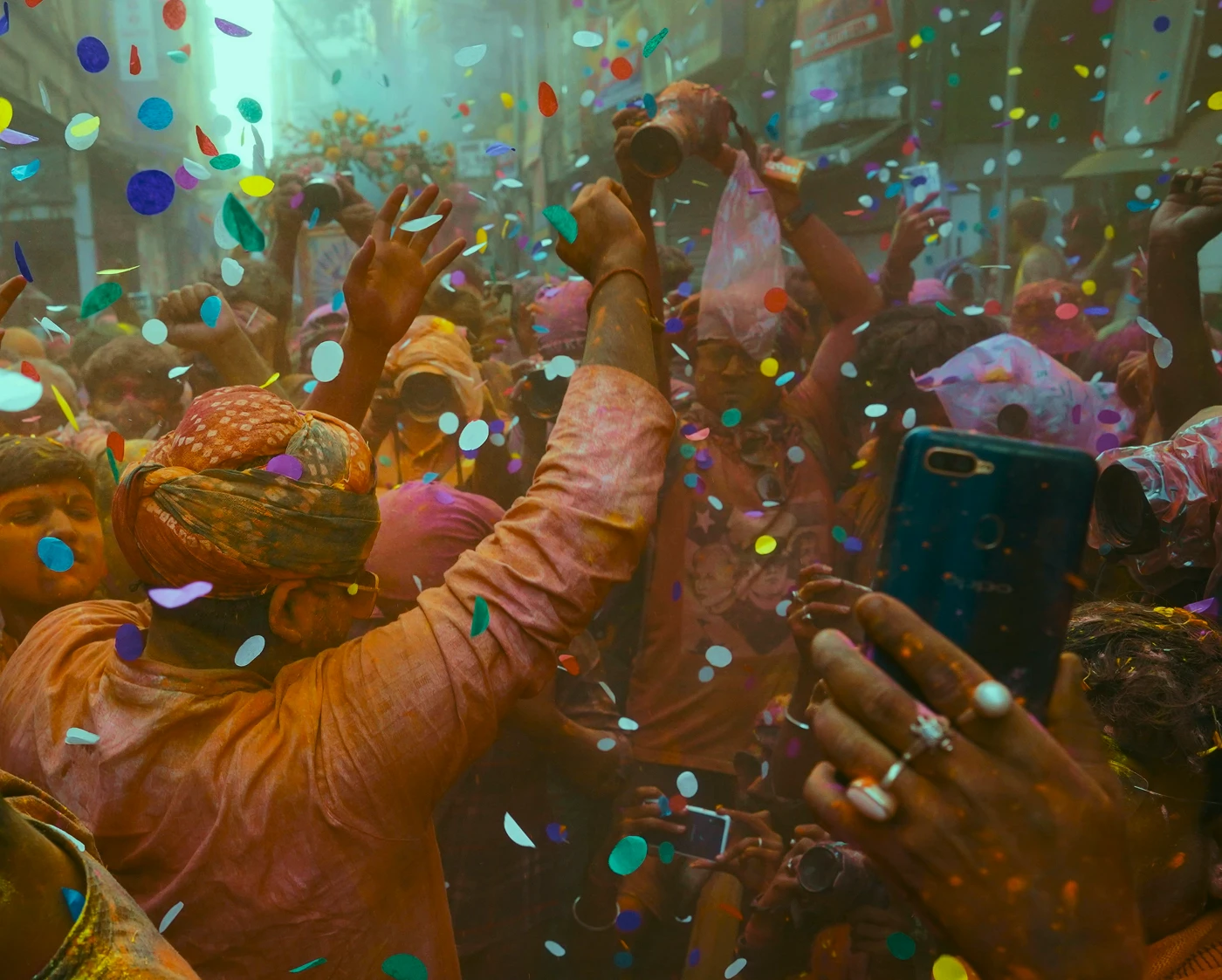 People celebrating Holi in the streets, with powder and confetti floating around them