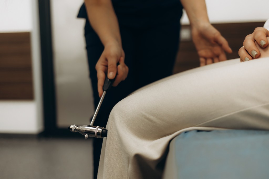 doctor knocks a hammer on the knee of a patient during neurological examination