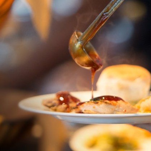 汤汁被淋到一盘食物上，食物包括一个面包卷和肉，盘中飘散着蒸汽。