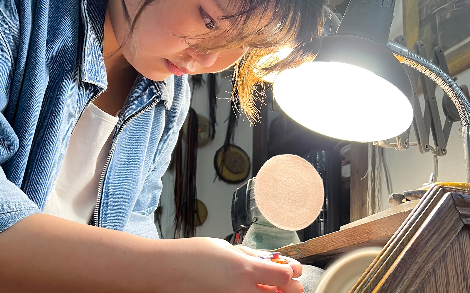 Person crafting amber jewelry under a lamp at Gdańsk Amber Workshop.