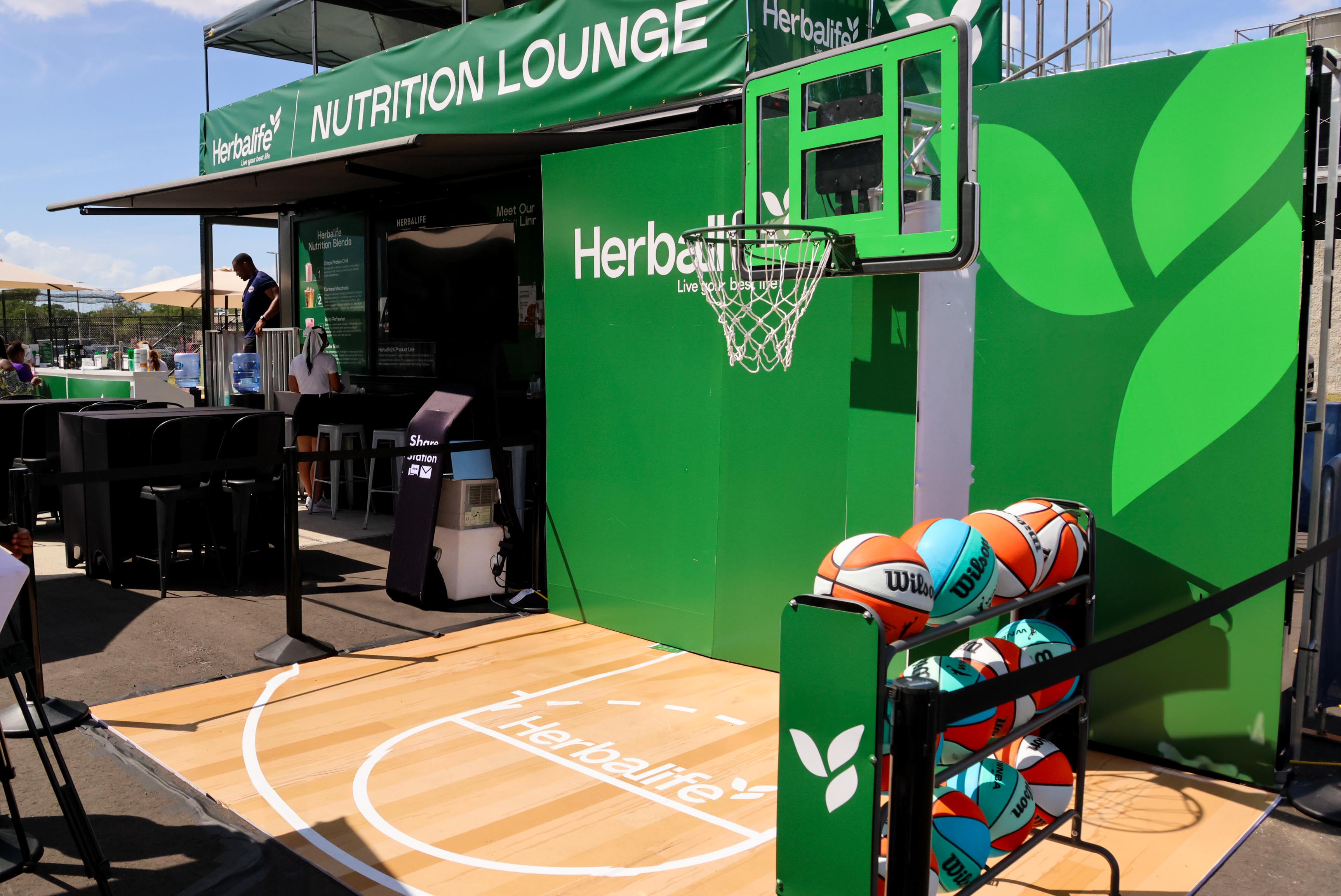 Basketball activation inside the Herbalife Nutrition Lounge with a hoop setup and rack of basketballs.