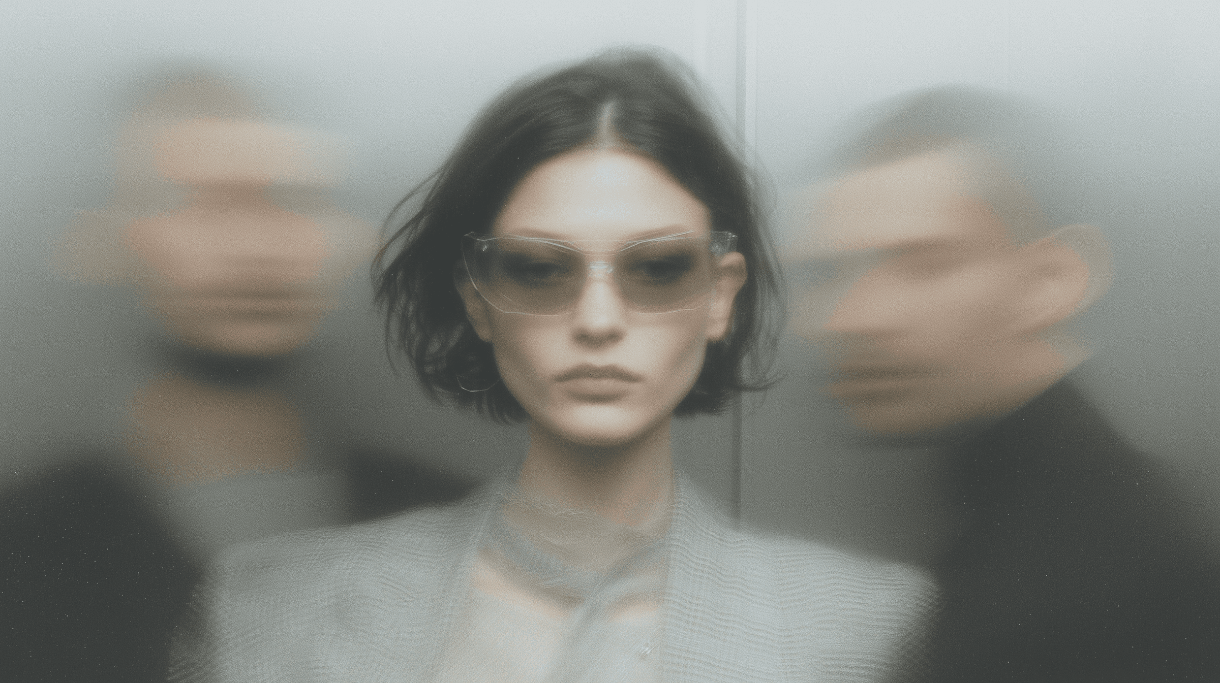 Woman with dark bob wearing transparent-frame sunglasses in focus, flanked by two heavily blurred figures on either side