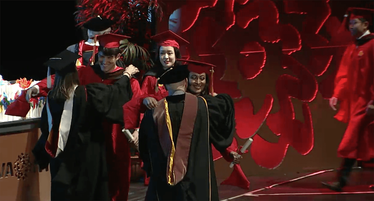 A photo of a couple of grad students and teachers, dressed in SVA color robes, that are hugging and congratulating each other.