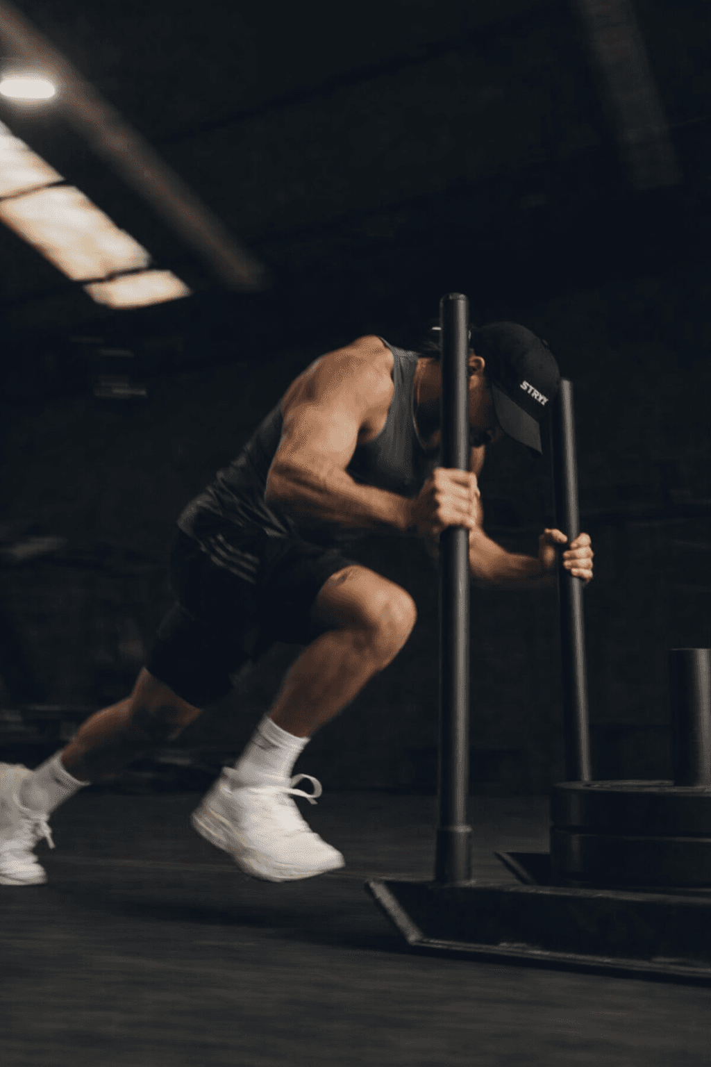 A person pushing a sled in a dimly lit gym, focused on strength training, wearing athletic gear.