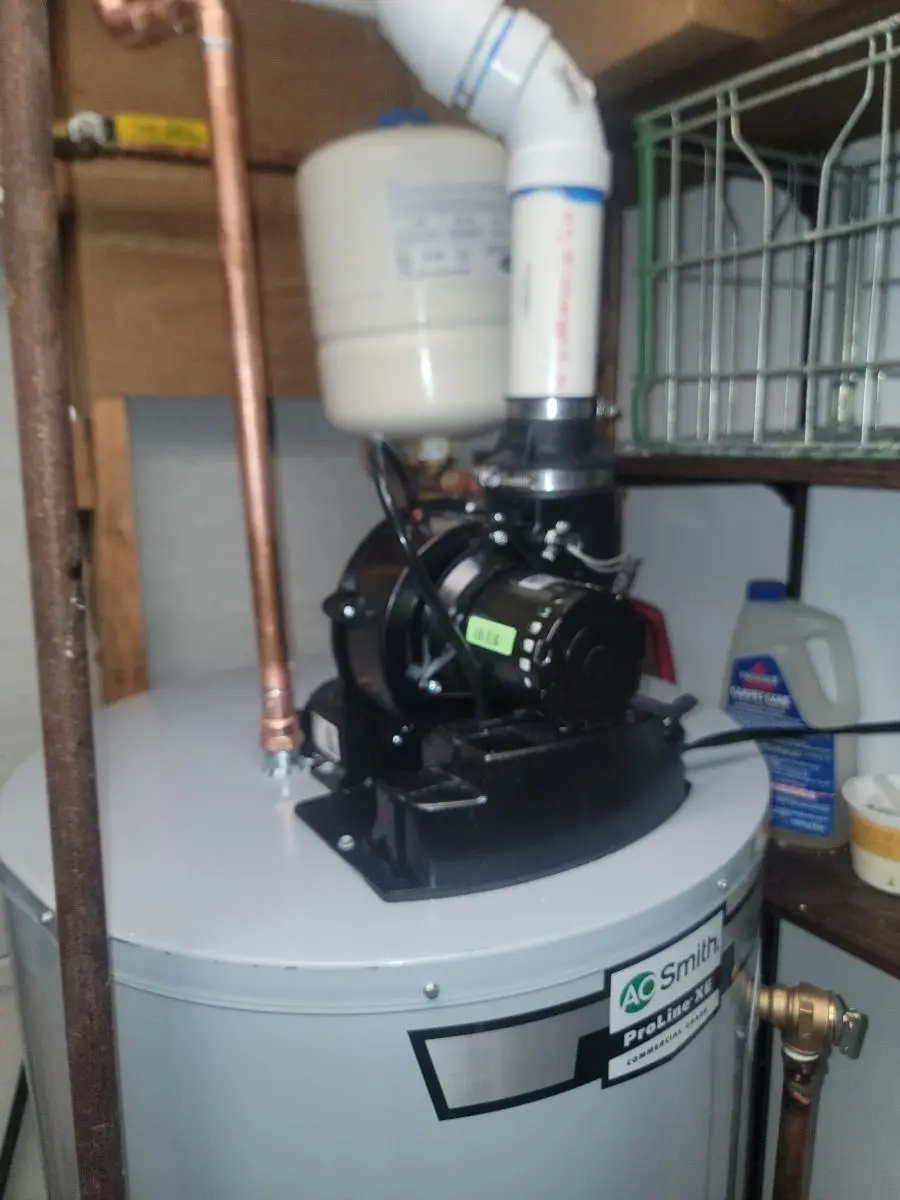 A professional gas water heater installation featuring a power vent blower motor, PVC exhaust piping, and a thermal expansion tank.