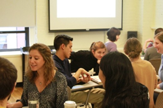 A group of people sitting in a classroom and in the background a screen projector.