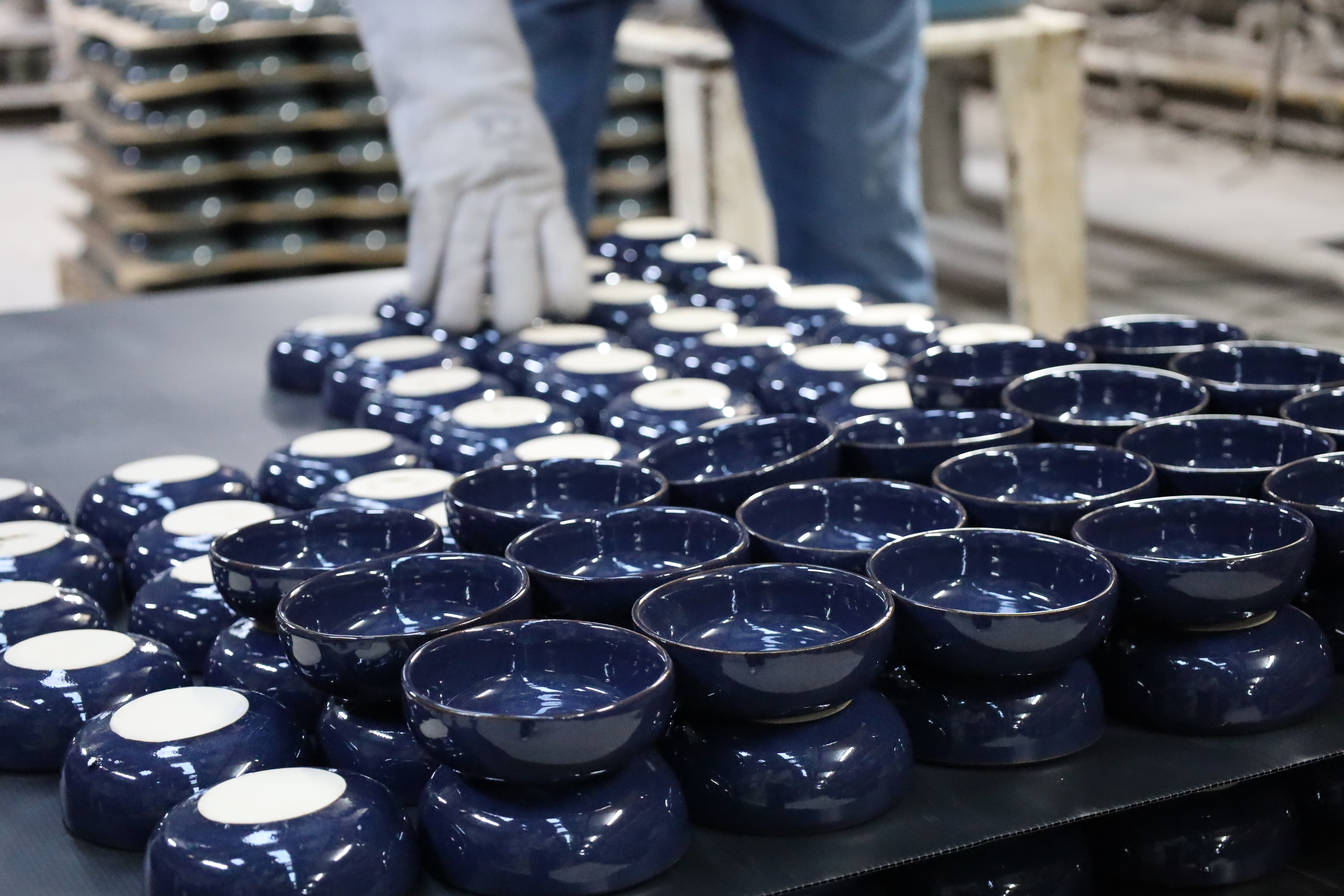 Opérateur en gants manipulant des bols en céramique émaillée bleu marine sortant de production sur une table d'atelier