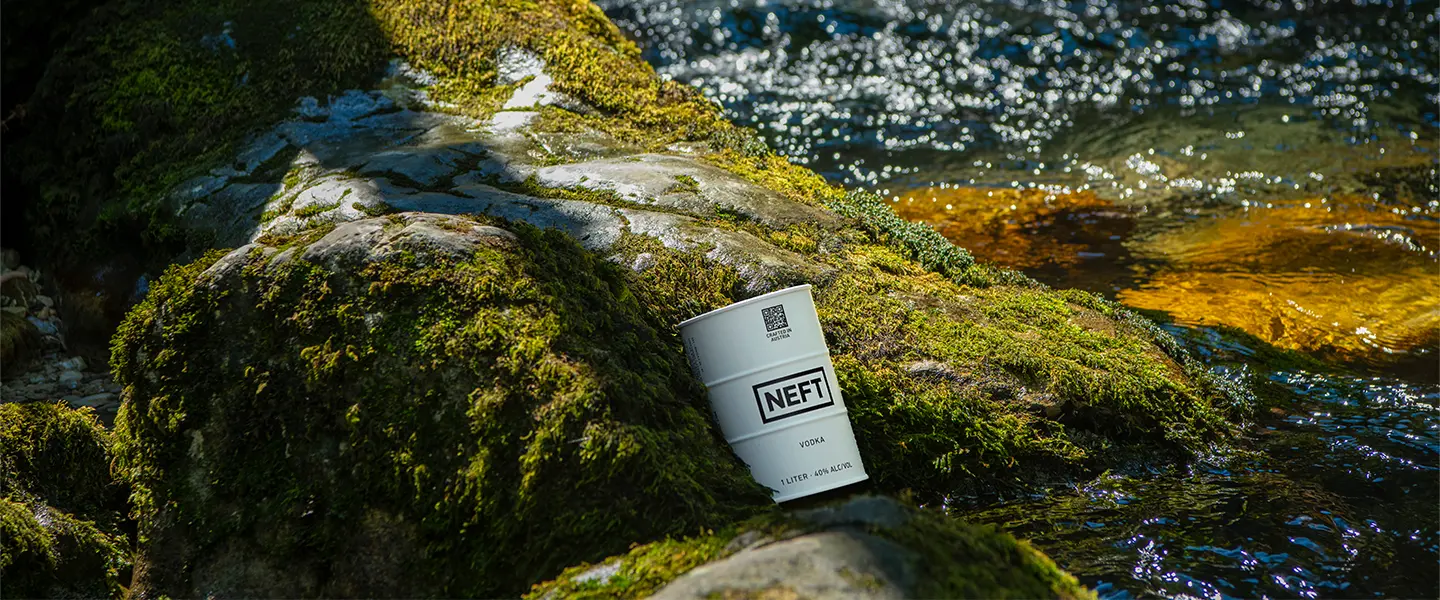 A NEFT Vodka white barrel laying gently on mossy rocks along a stream of water.