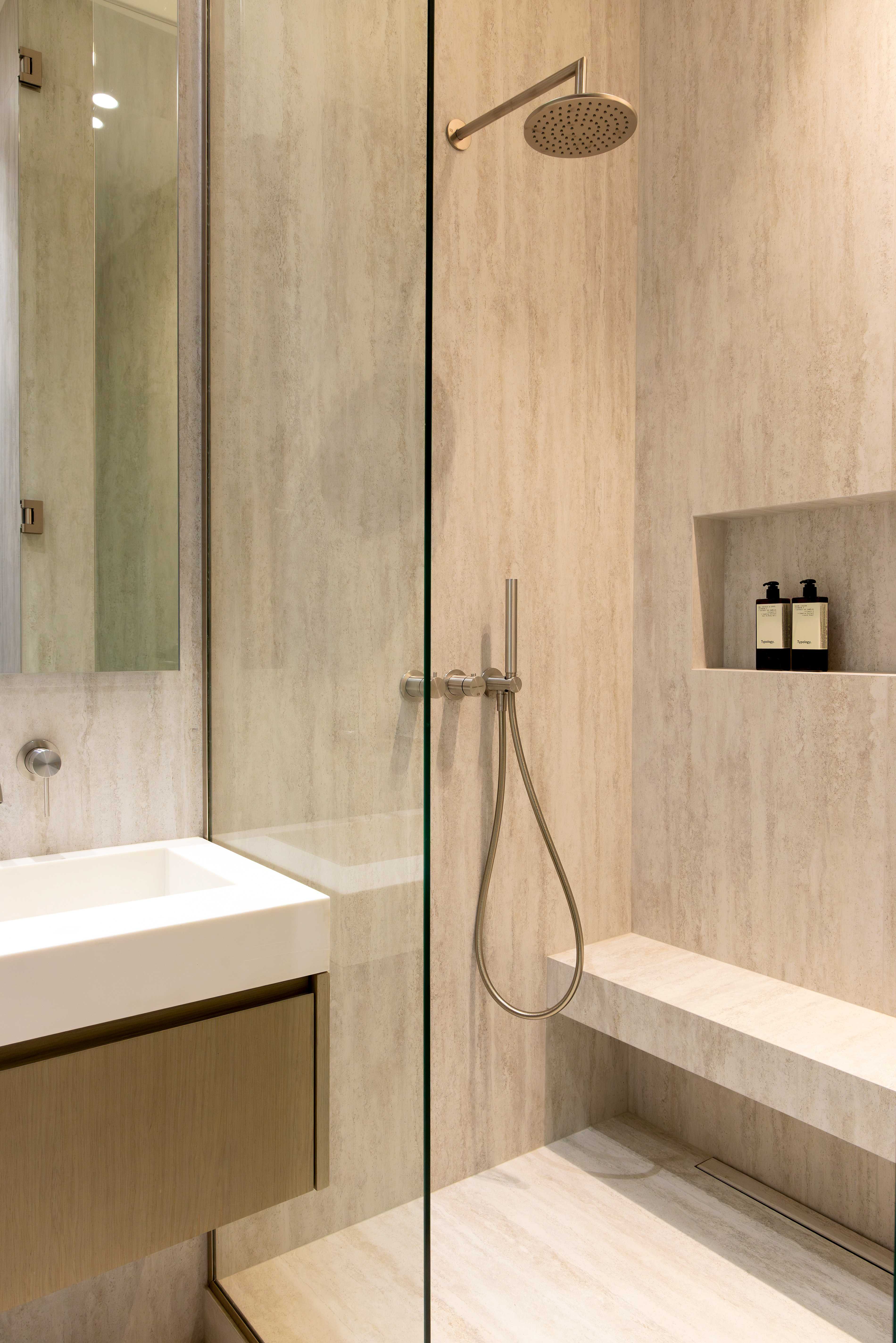 Douche italienne en travertin avec paroi vitree, pommeau de douche et banc integre avec niche de produits