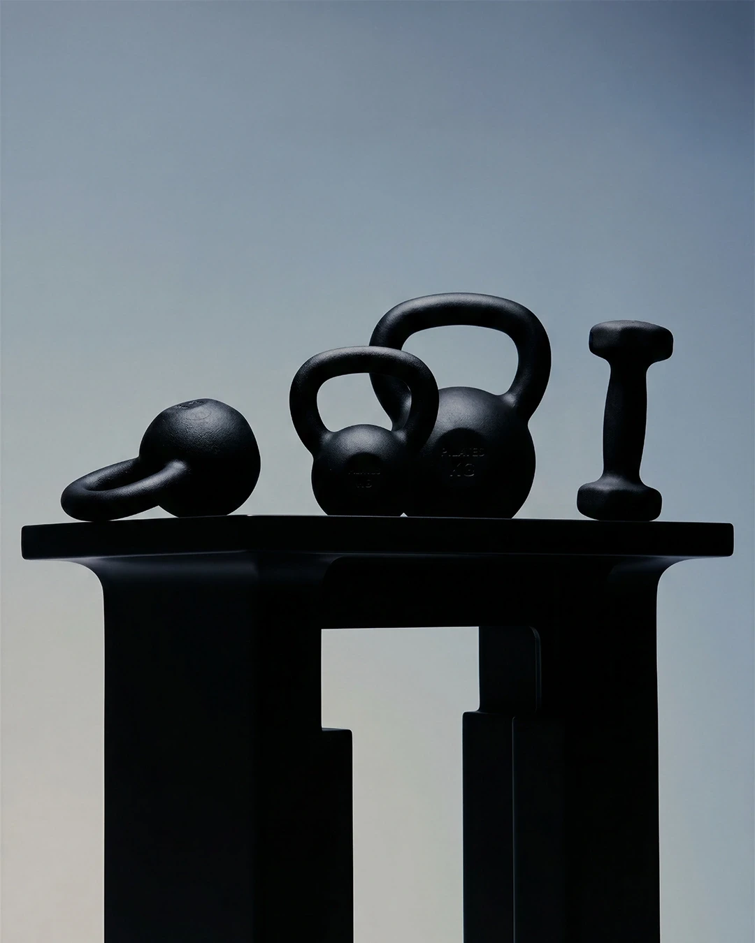 A sleek arrangement of black kettlebells and a dumbbell on a modern surface, set against a gradient blue background.