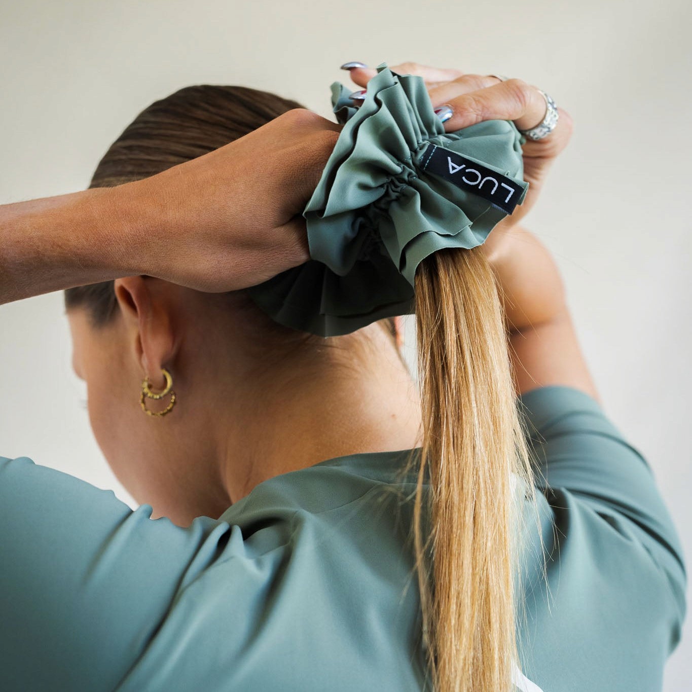 Cyclist wearing LUCA Uplift scrunchie in matcha holding a ponytail, back view