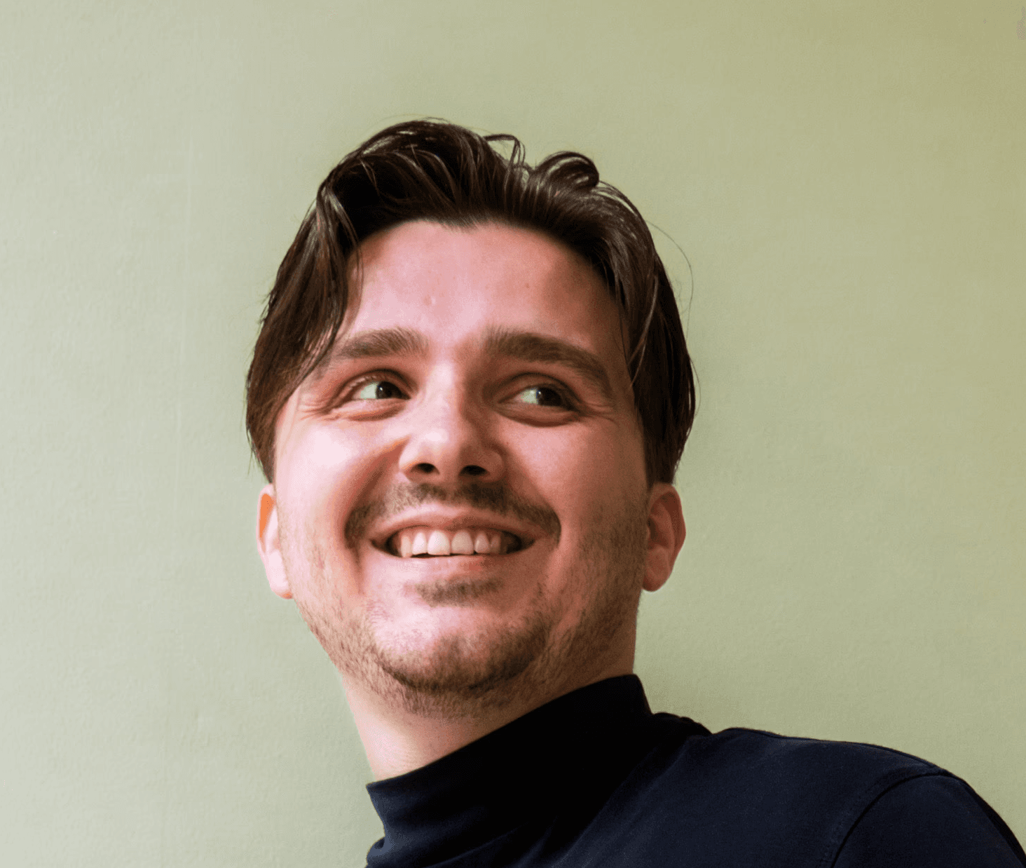 Profilfoto einer lächelnden Person in schwarzer Kleidung vor einem grünen Hintergrund