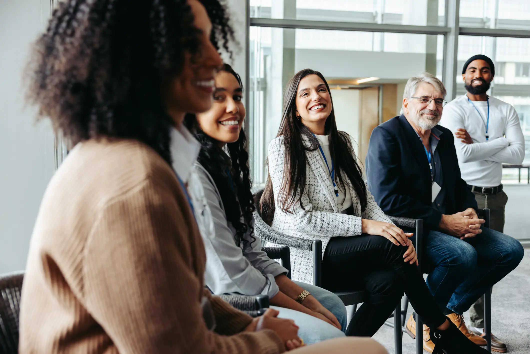 Diverse group of business professionals wearing lanyards seated together in an engaged workshop discussion, smiling and listening attentively